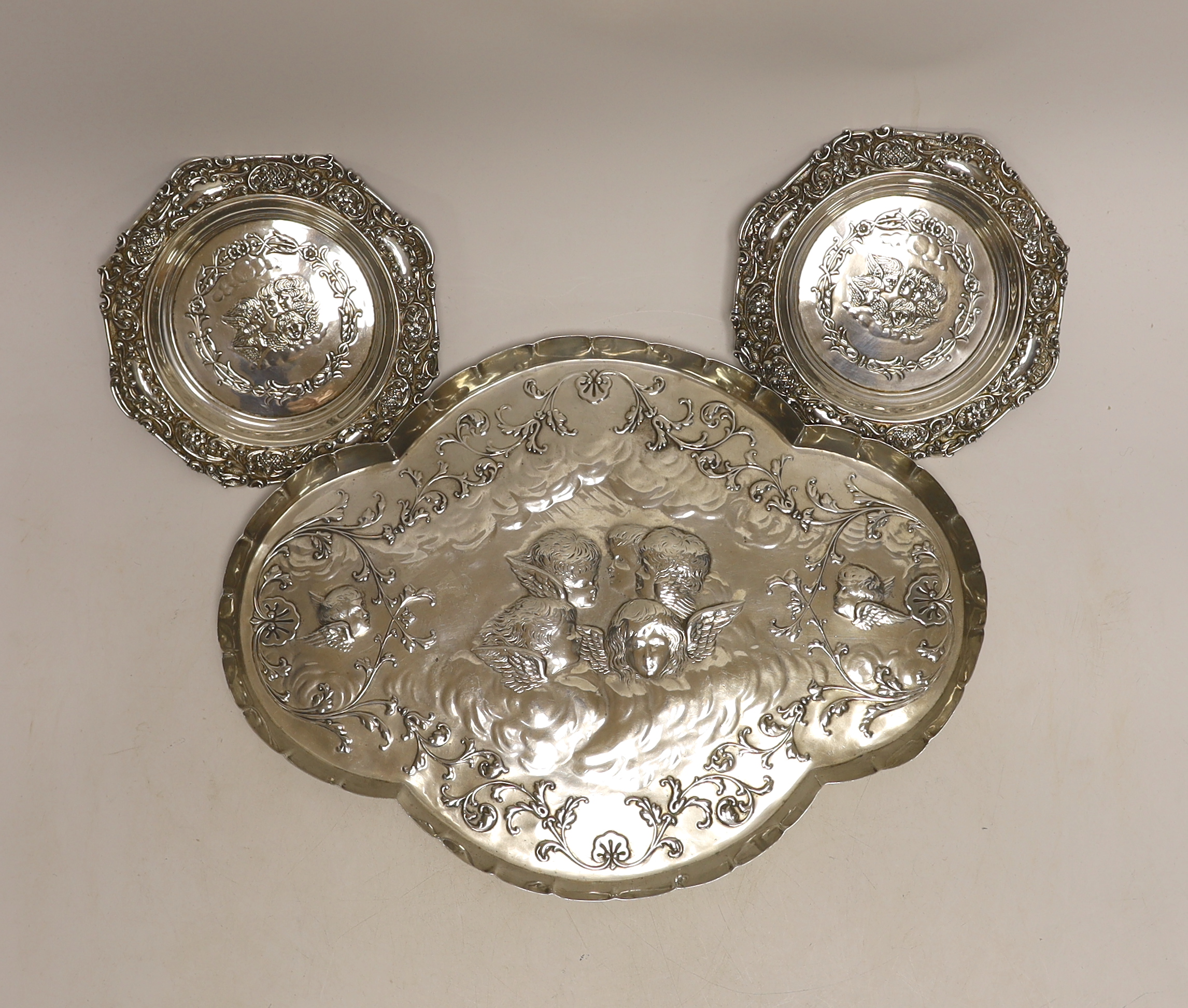 A late Victorian repousse silver dressing table tray with Reynold's Angels decoration, William Comyns, London, 1899, 30.9cm and a pair of smaller similar dishes by Henry Matthews, Birmingham, 1899, 14.2oz.